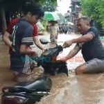 Foto: Sejumlah warga saat mengevakuasi motor yang sempat terbawa arus dan terkubur jalanan rusak akibat arus air banjir sangat deras, Minggu (9/1/2022).